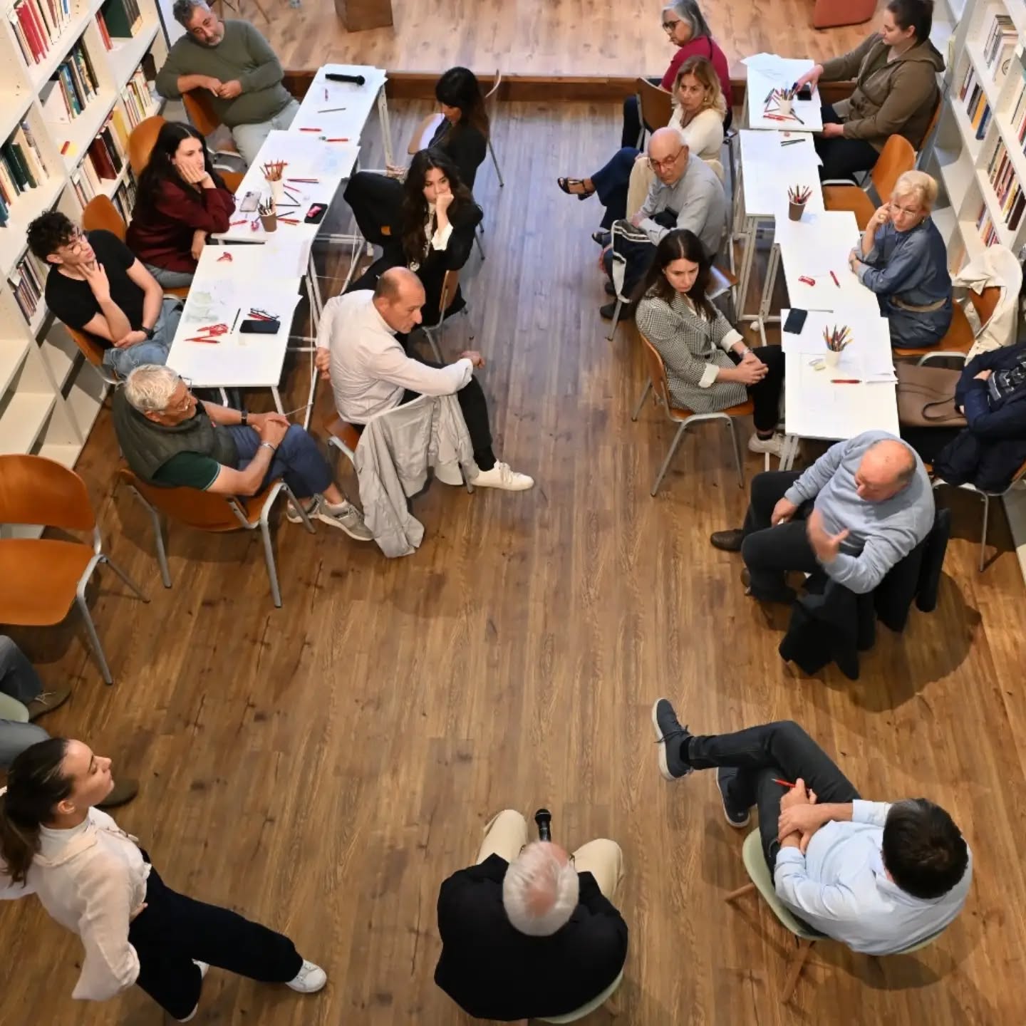 Overhead view of workshop participants seated in a circle of tables in a library, drawing and talking together