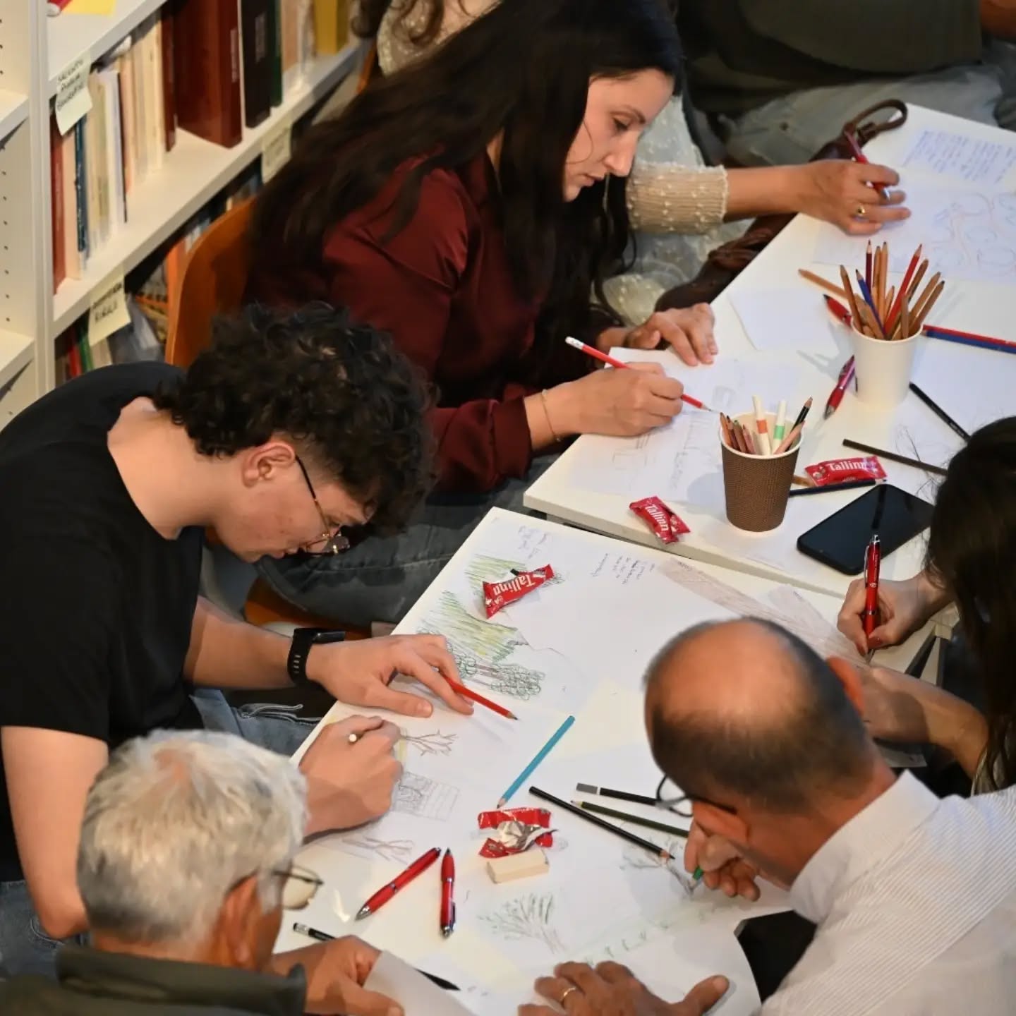 Participants at a table drawing their childhood places in pencil and colour, surrounded by library shelves