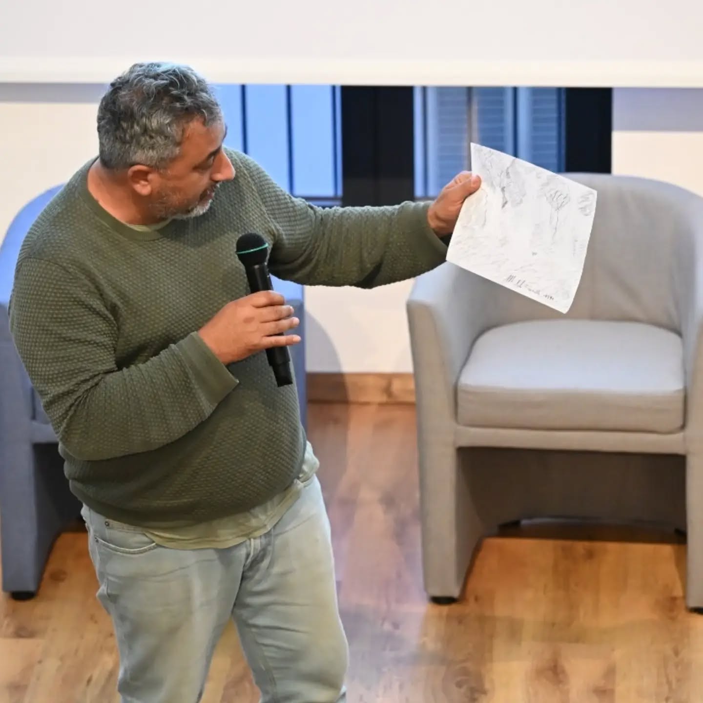 A workshop participant holding up his drawing and speaking into a microphone, telling the group the story behind it